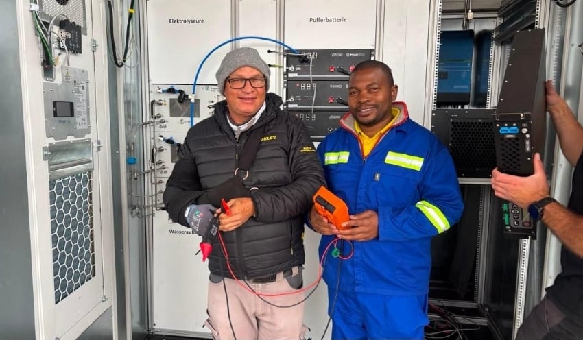 Green hydrogen technology being tested at Kalahari Anib Lodge, with two technicians standing inside the containerised electrolyser and energy storage system.